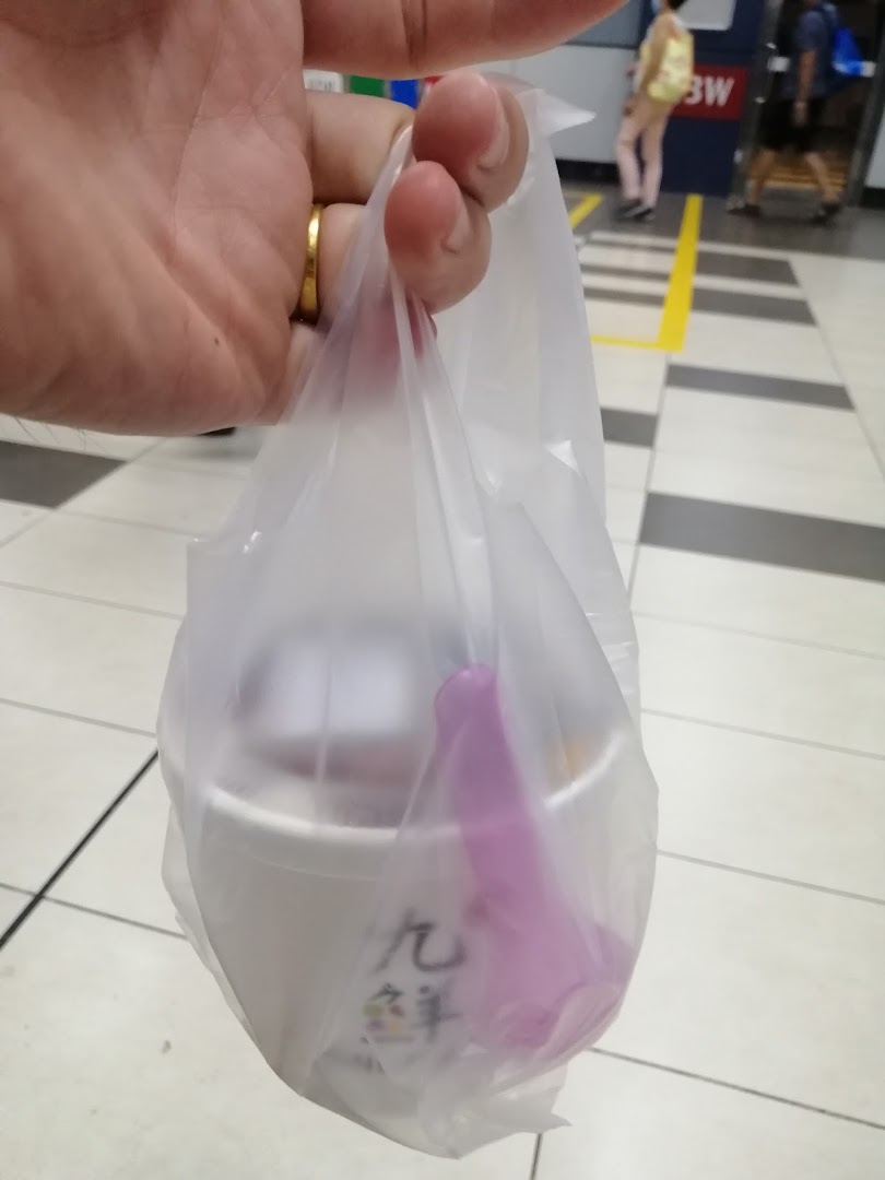 A hand holds a plastic bag containing a Nine Fresh dessert cup and a purple spoon.