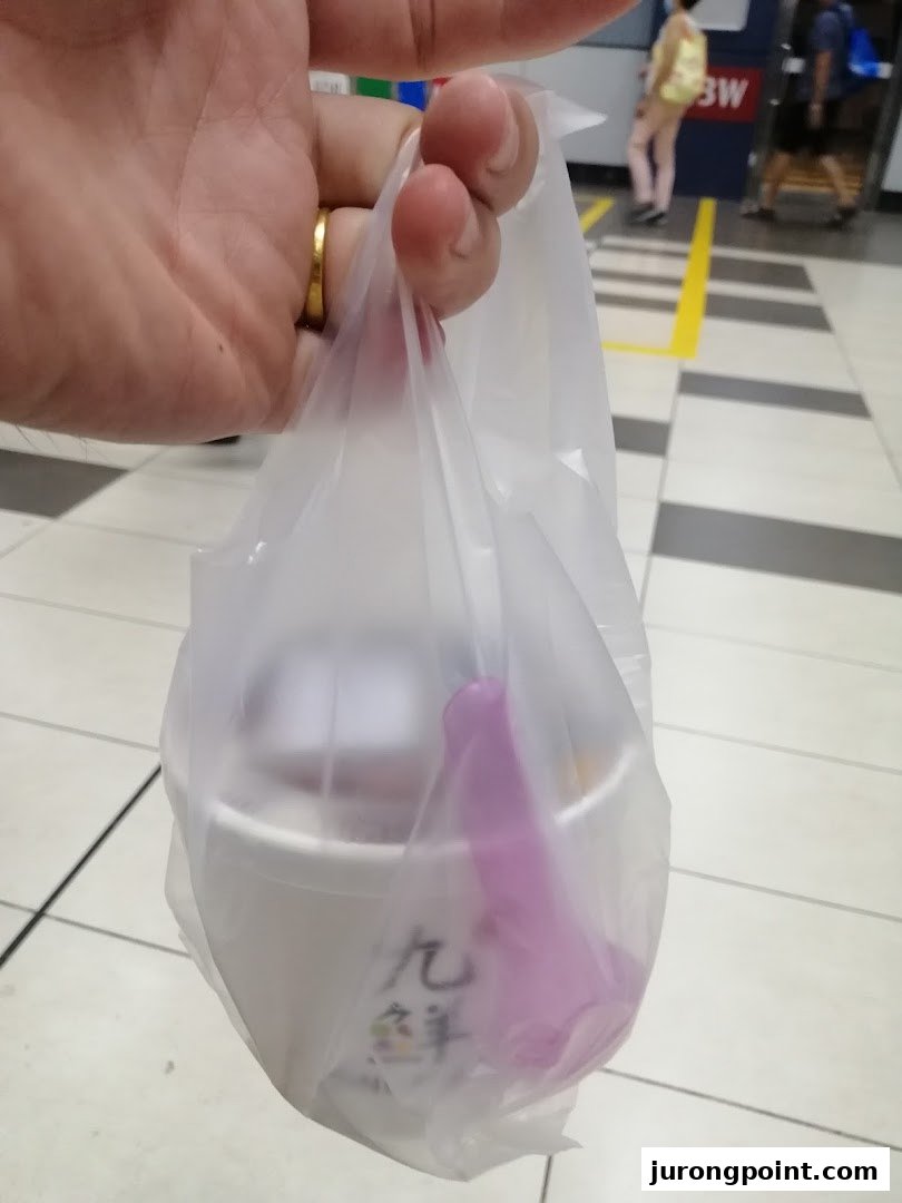 A hand holds a plastic bag containing a Nine Fresh dessert cup and a purple spoon.