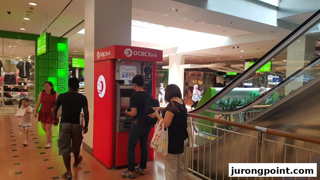 People are using a red OCBC ATM located inside a bustling shopping mall.