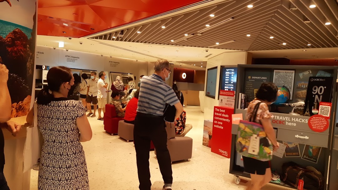 Customers inside OCBC Bank Jurong Point, featuring ATMs and a travel-themed promotional display.