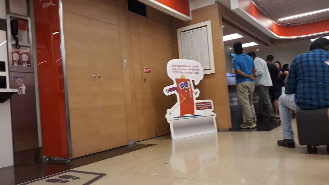 Interior view of OCBC Bank with customers, self-service kiosks, and promotional displays.