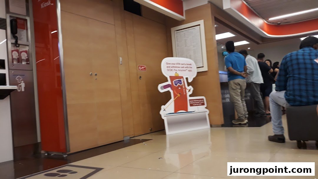 Interior view of OCBC Bank with customers, self-service kiosks, and promotional displays.