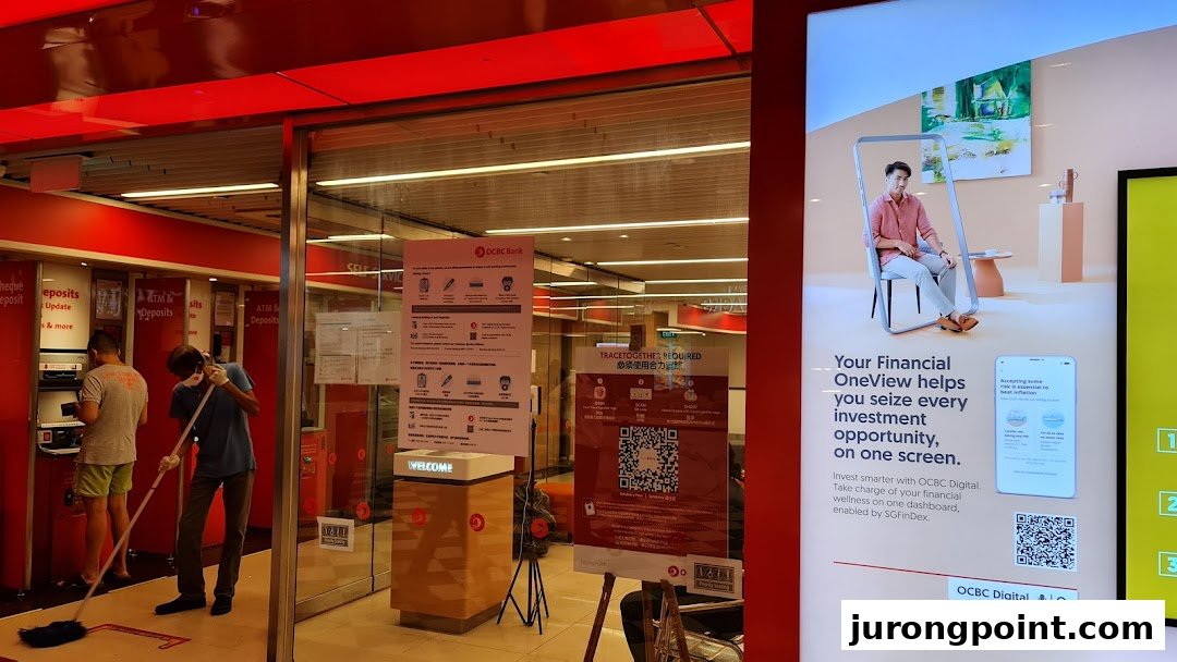 The entrance of OCBC Bank with ATMs, staff cleaning, and a digital financial services advertisement.