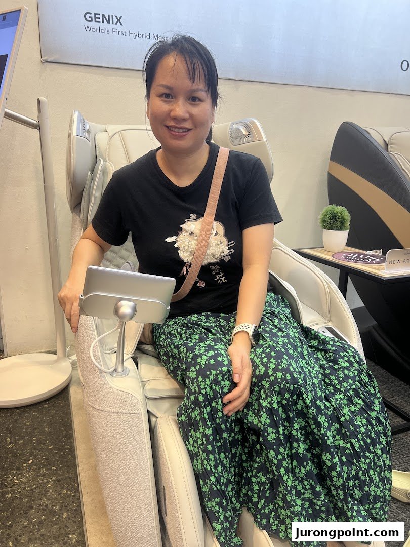 A woman smiling while trying out a massage chair at OGAWA, featuring a 'GENIX' model.