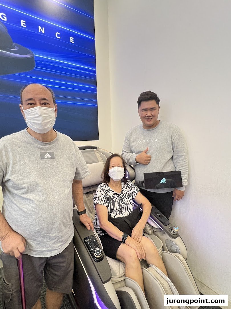 Customers and staff interacting with a massage chair inside the Ogawa store.