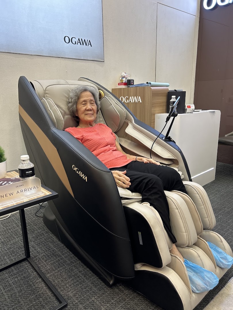 An elderly woman comfortably testing a luxurious massage chair inside an OGAWA retail store.