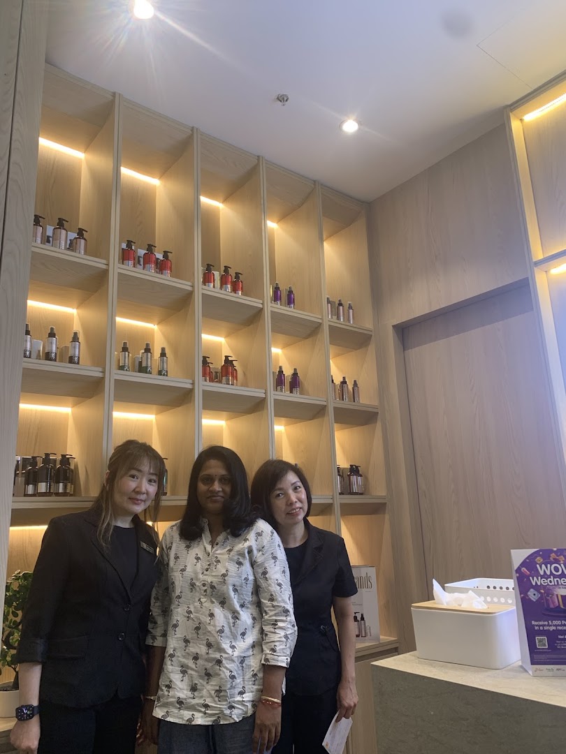 Three people, likely staff and a customer, stand in a modern hair solutions shop with product displays.