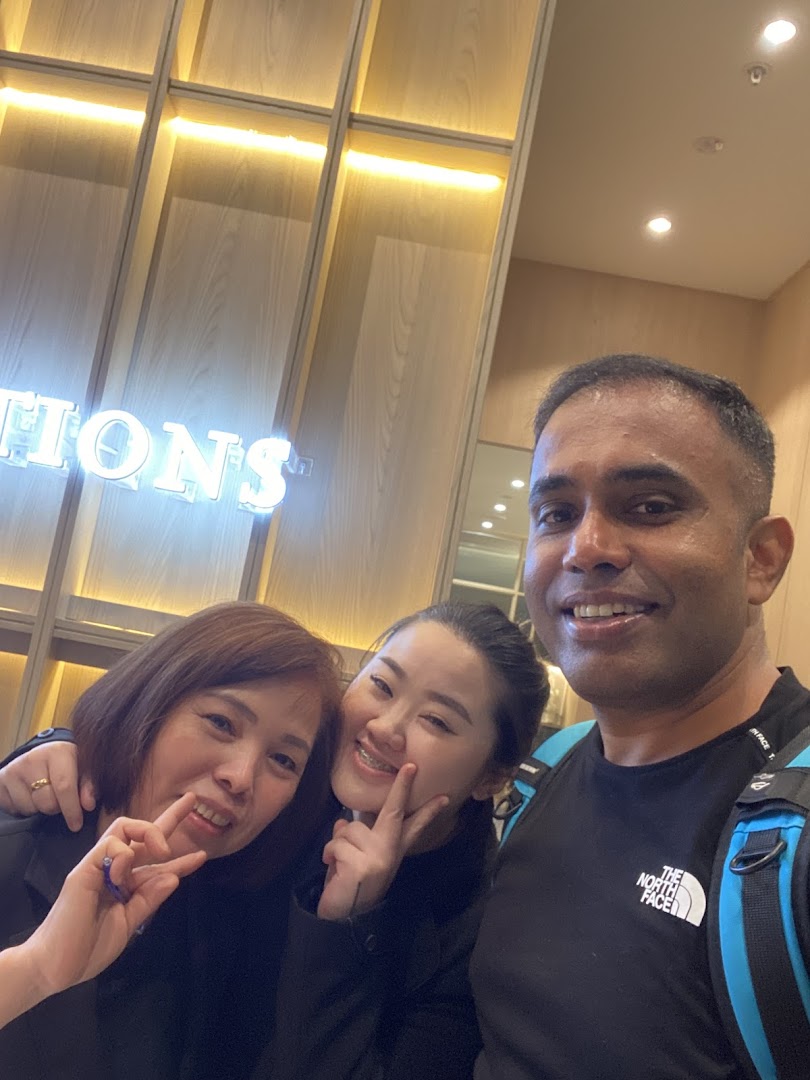 Three smiling individuals posing in front of a neon sign for 'Oriental Hair Solutions'.