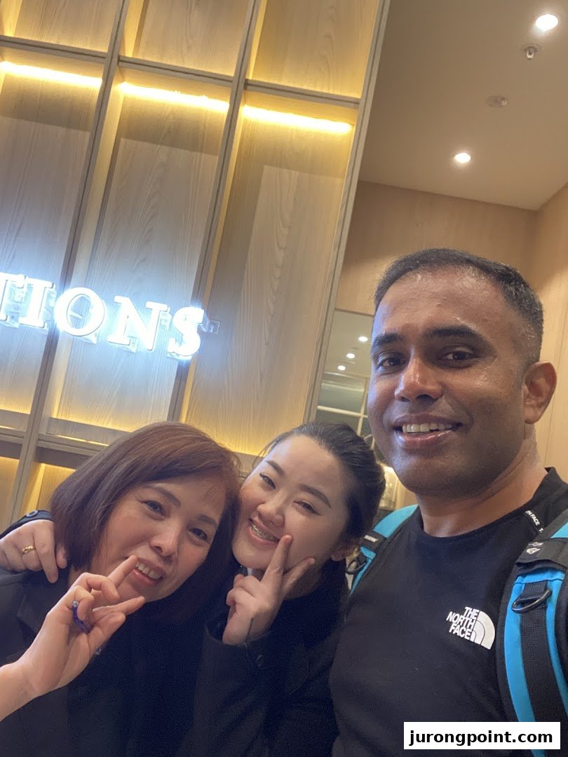 Three smiling individuals posing in front of a neon sign for 'Oriental Hair Solutions'.