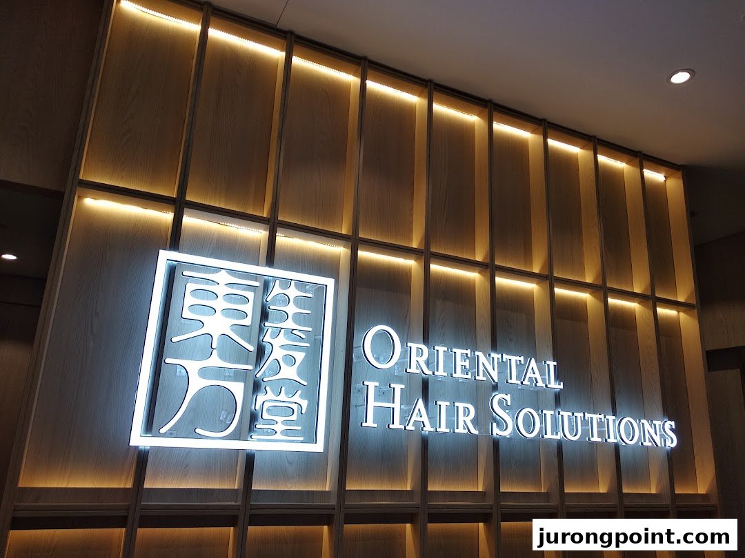 The illuminated sign for 'Oriental Hair Solutions' on a stylish wooden wall.