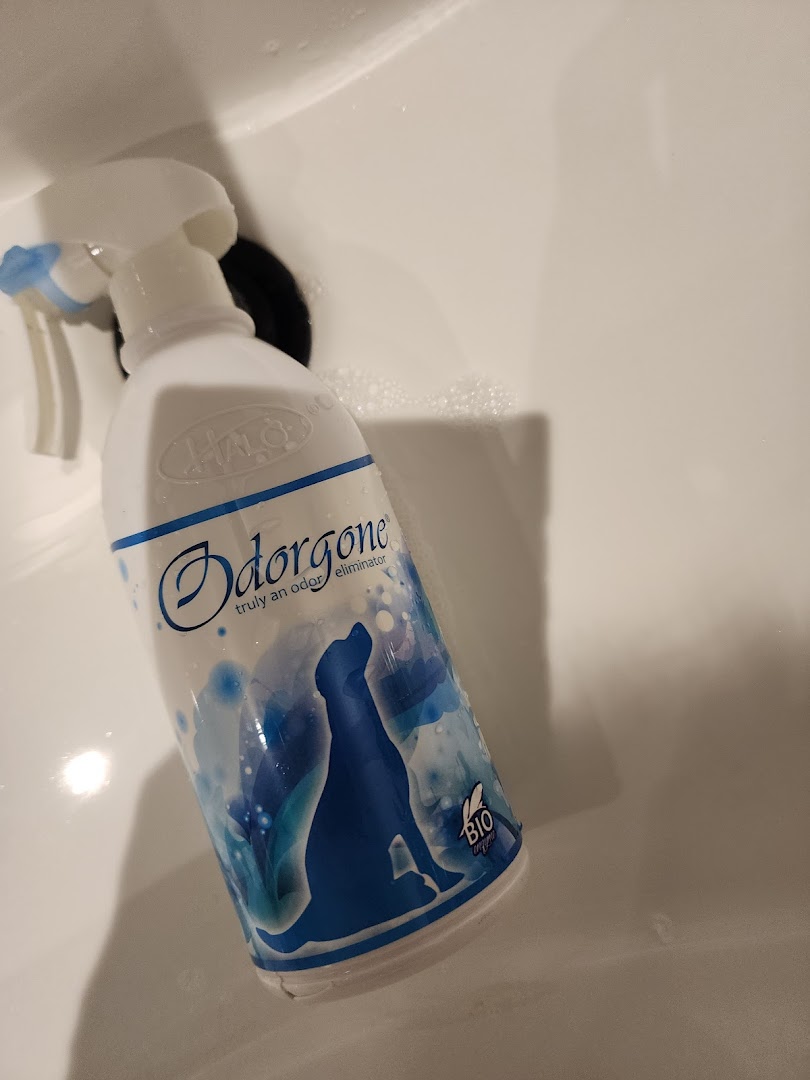 A bottle of Odorgone pet odor eliminator spray with a dog silhouette design in a white sink.