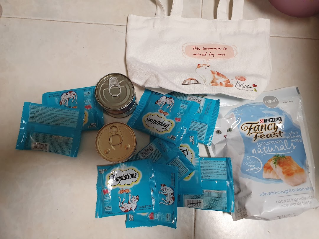 An assortment of cat food products including Temptations treats, Fancy Feast, and a Pets Station tote bag.