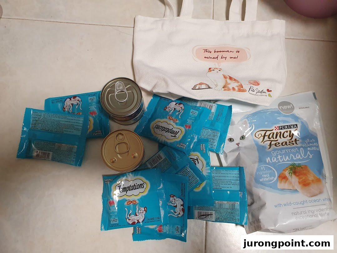 An assortment of cat food products including Temptations treats, Fancy Feast, and a Pets Station tote bag.