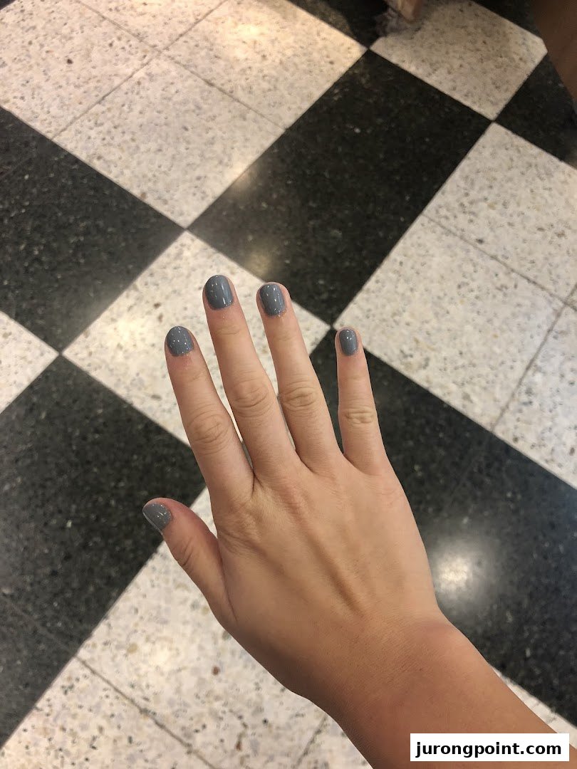 A hand with freshly painted grey nails against a black and white checkered floor.
