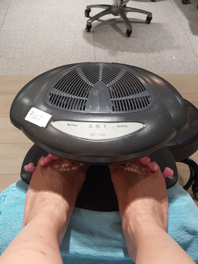 A customer's feet are under a nail dryer with toe separators at Pixie Nail Spa.