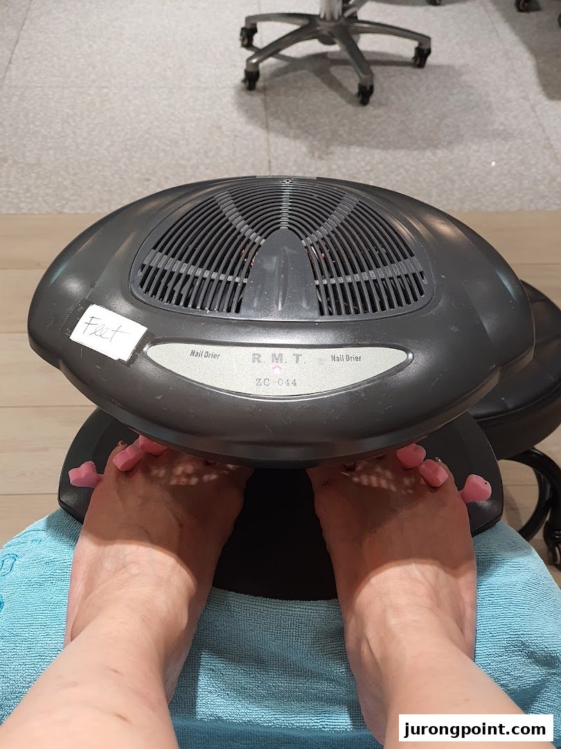 A customer's feet are under a nail dryer with toe separators at Pixie Nail Spa.