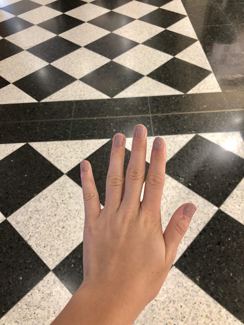 A hand with freshly painted light pink nails against a classic black and white checkered floor.
