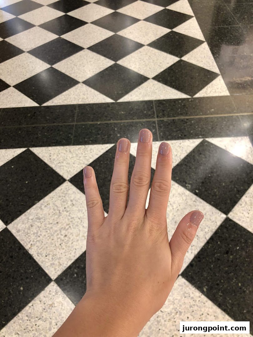 A hand with freshly painted light pink nails against a classic black and white checkered floor.