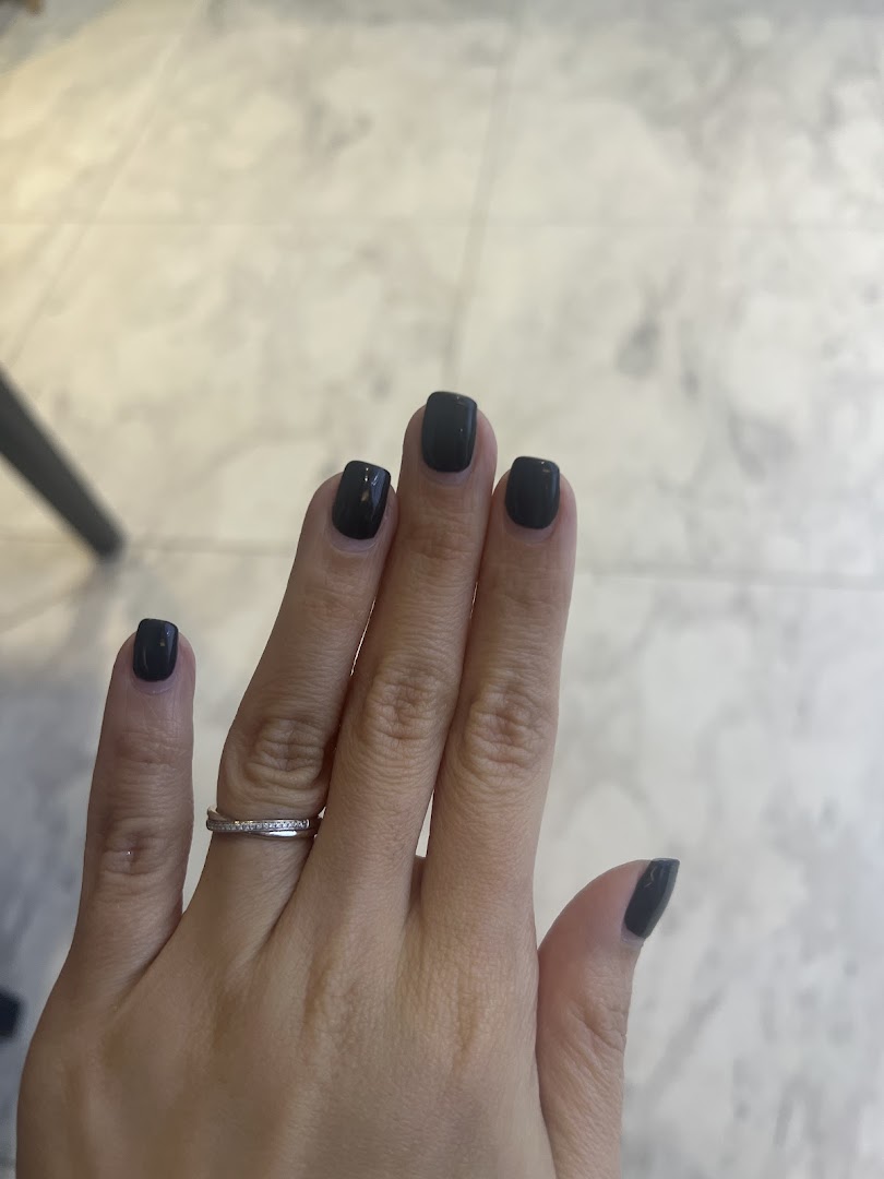 A hand with freshly painted dark grey nails and a silver ring, showcasing a nail spa service.