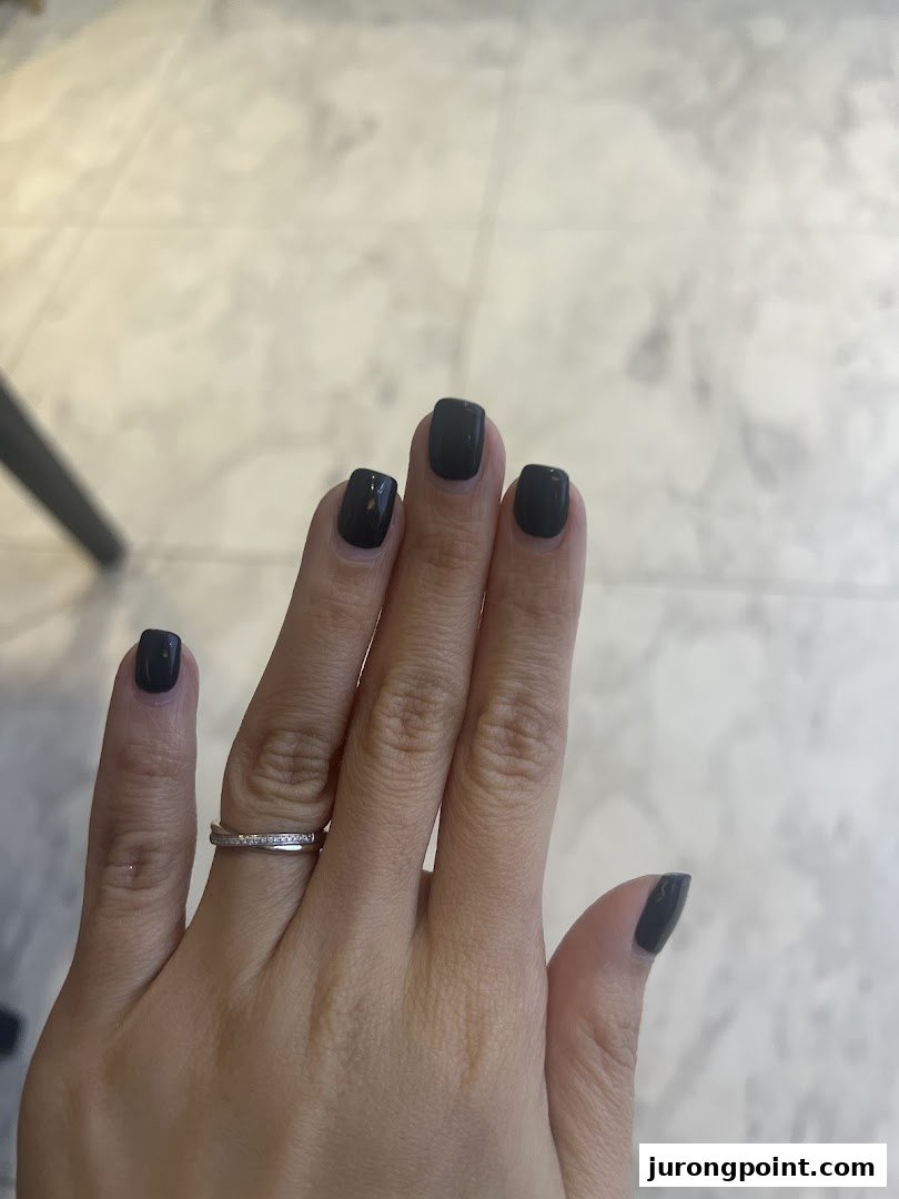 A hand with freshly painted dark grey nails and a silver ring, showcasing a nail spa service.