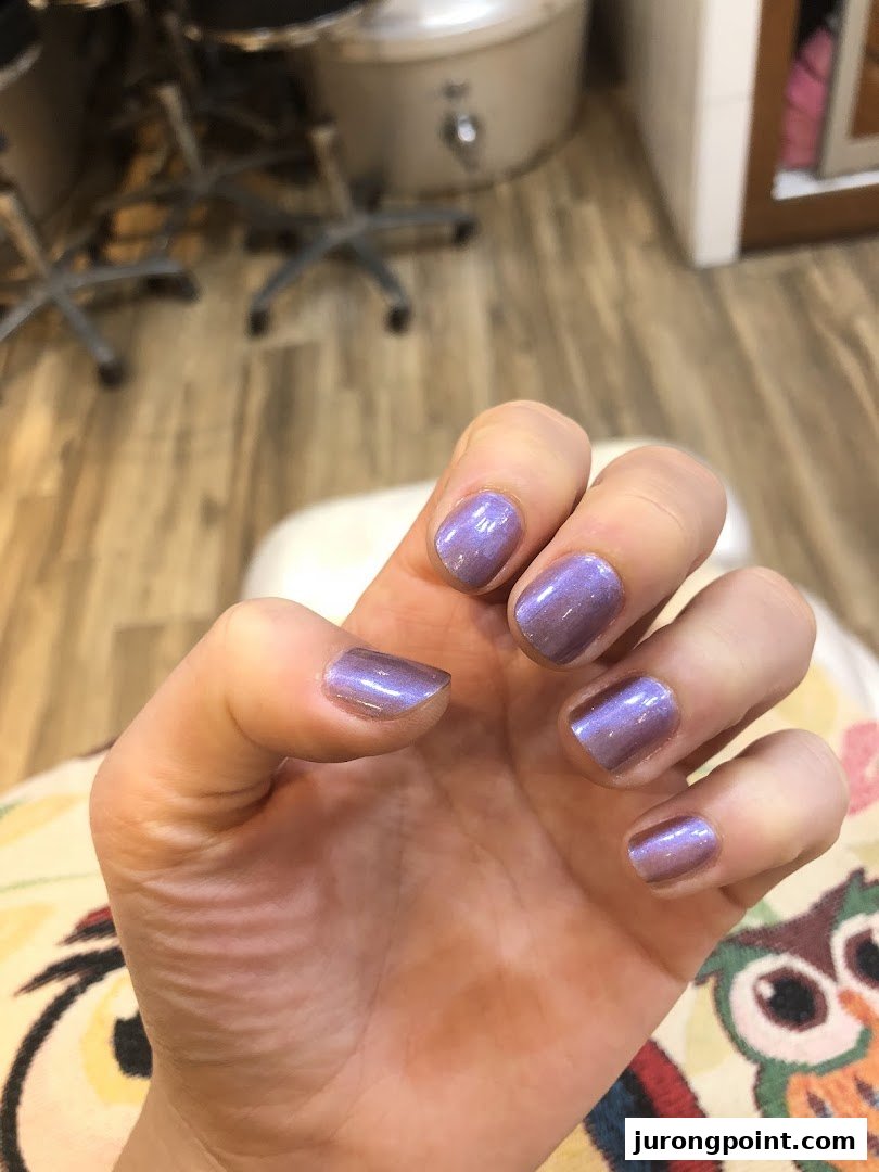 A hand showcasing freshly painted iridescent purple nails, highlighting a service from Pixie Nail Spa.