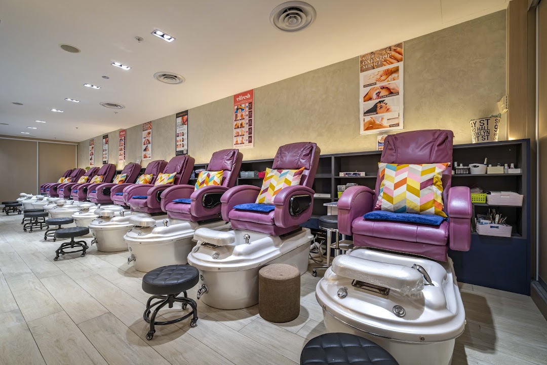 A row of comfortable purple pedicure chairs with foot baths and colorful pillows in a modern nail spa.