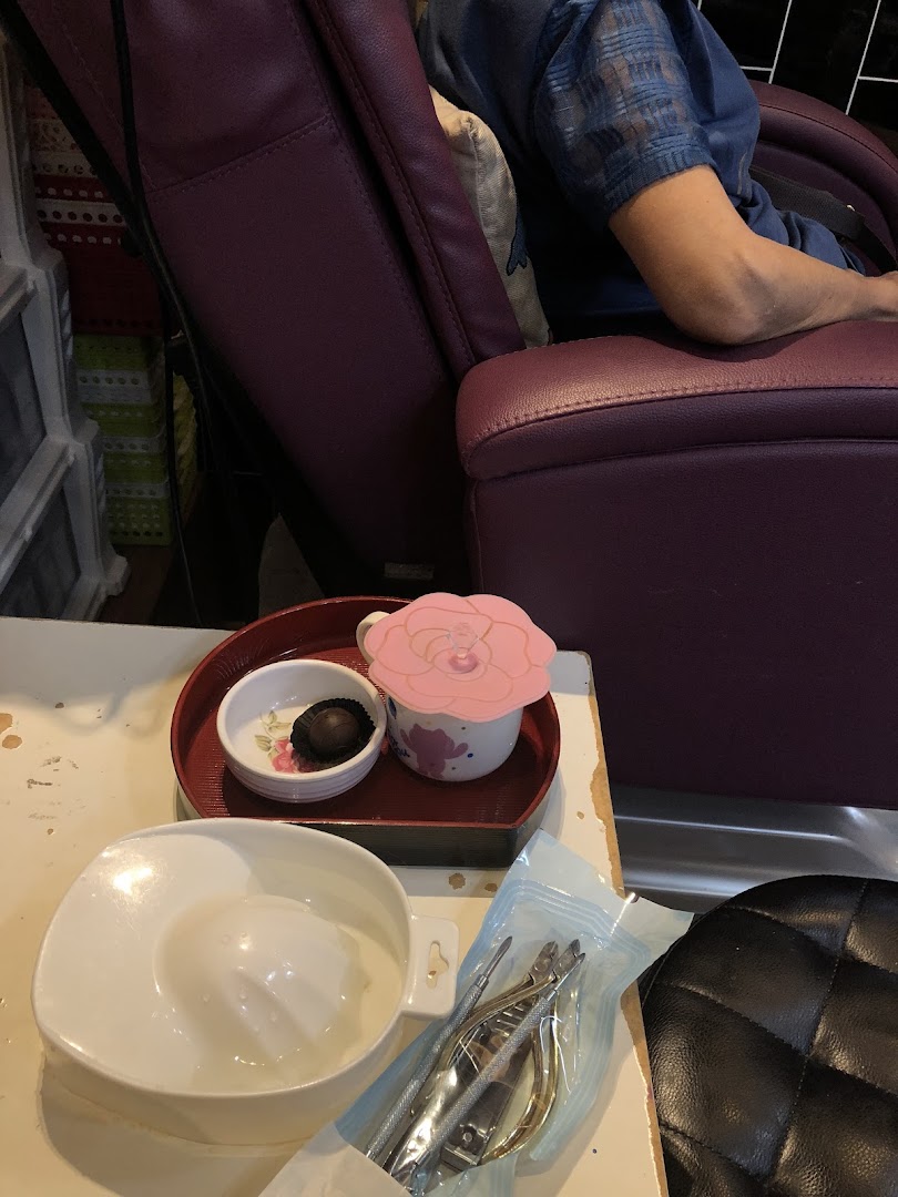 A client relaxing in a spa chair with nail tools, a drink, and a chocolate treat.