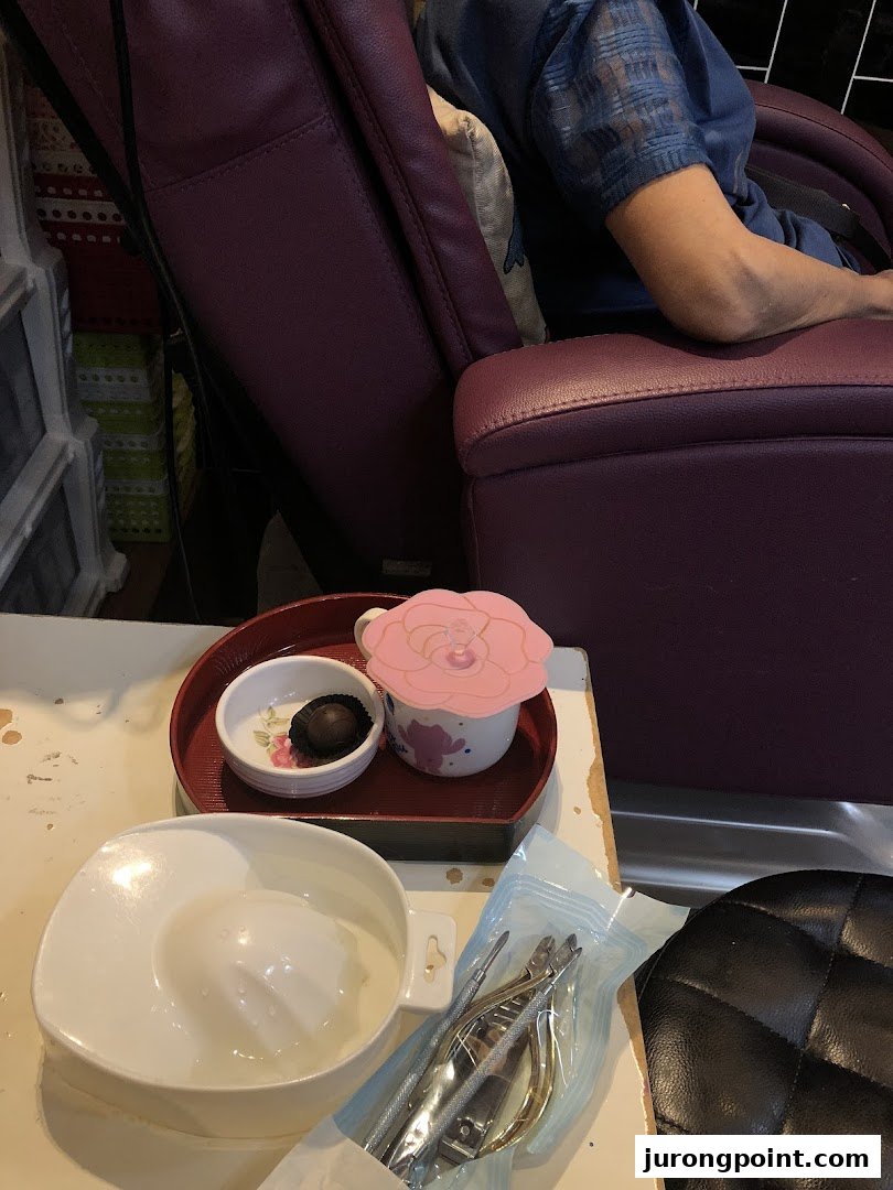 A client relaxing in a spa chair with nail tools, a drink, and a chocolate treat.