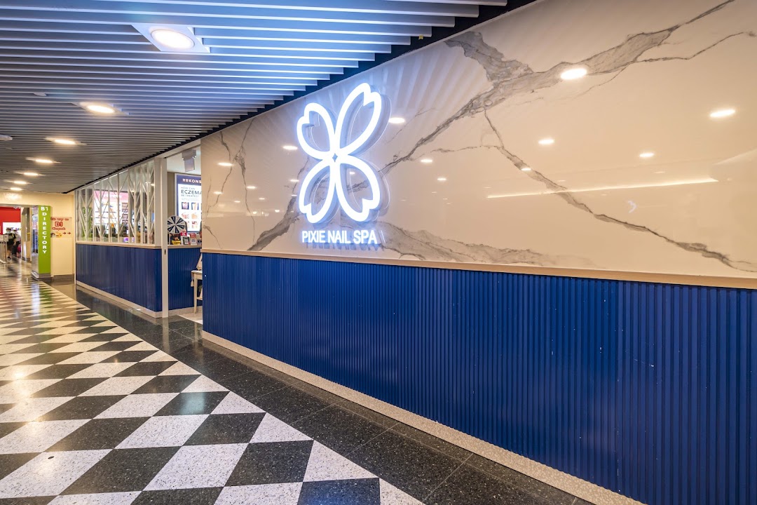 The vibrant blue and white storefront of Pixie Nail Spa, featuring its glowing floral logo in a mall corridor.