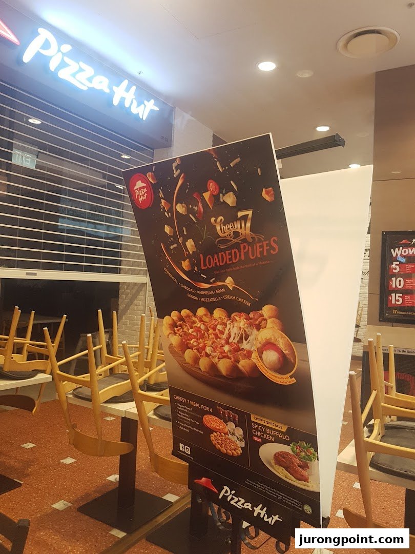 An interior view of Pizza Hut featuring a promotional stand for Cheesy Loaded Puffs and Spicy Buffalo Chicken.