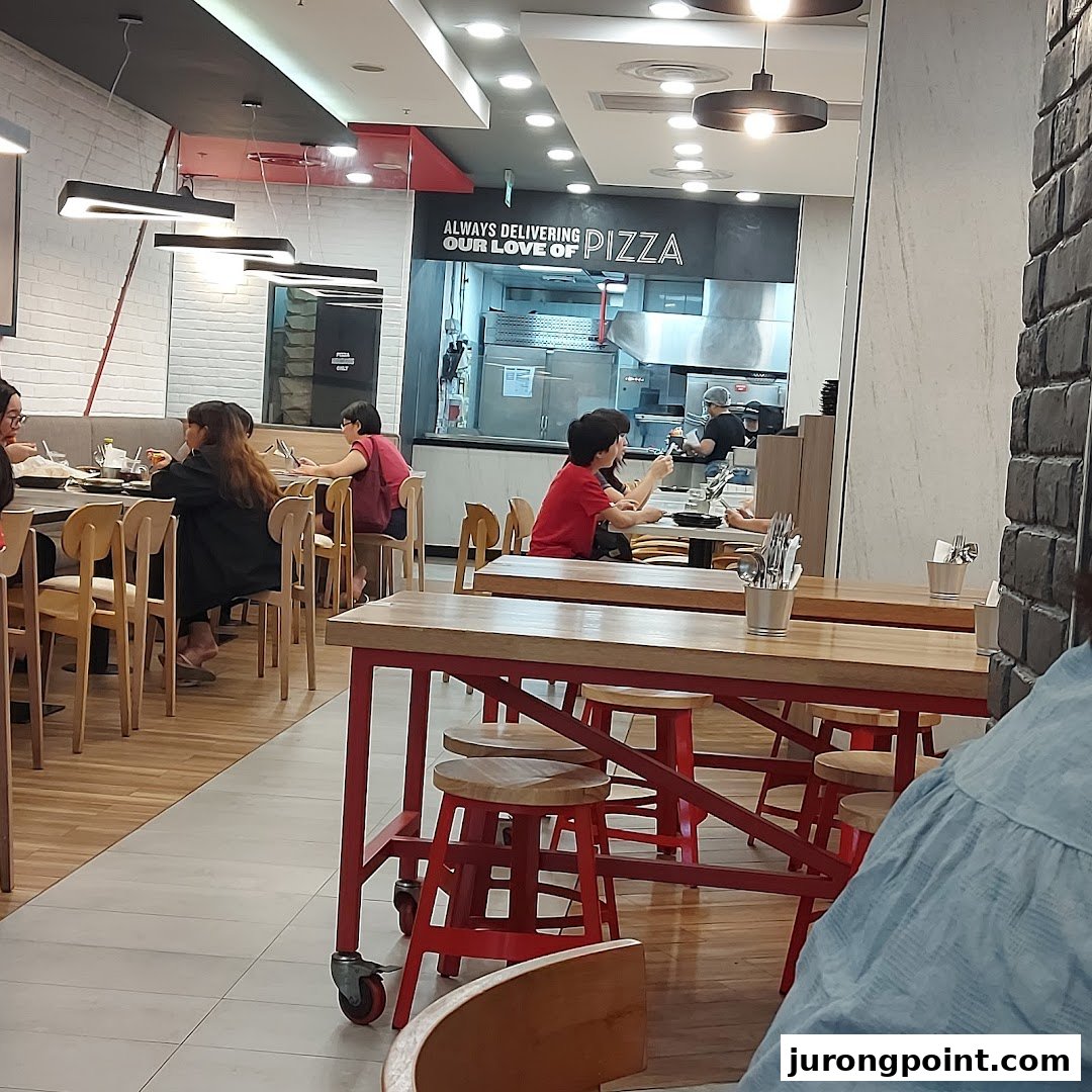 Diners enjoy a meal inside Pizza Hut, with the open kitchen visible in the background.