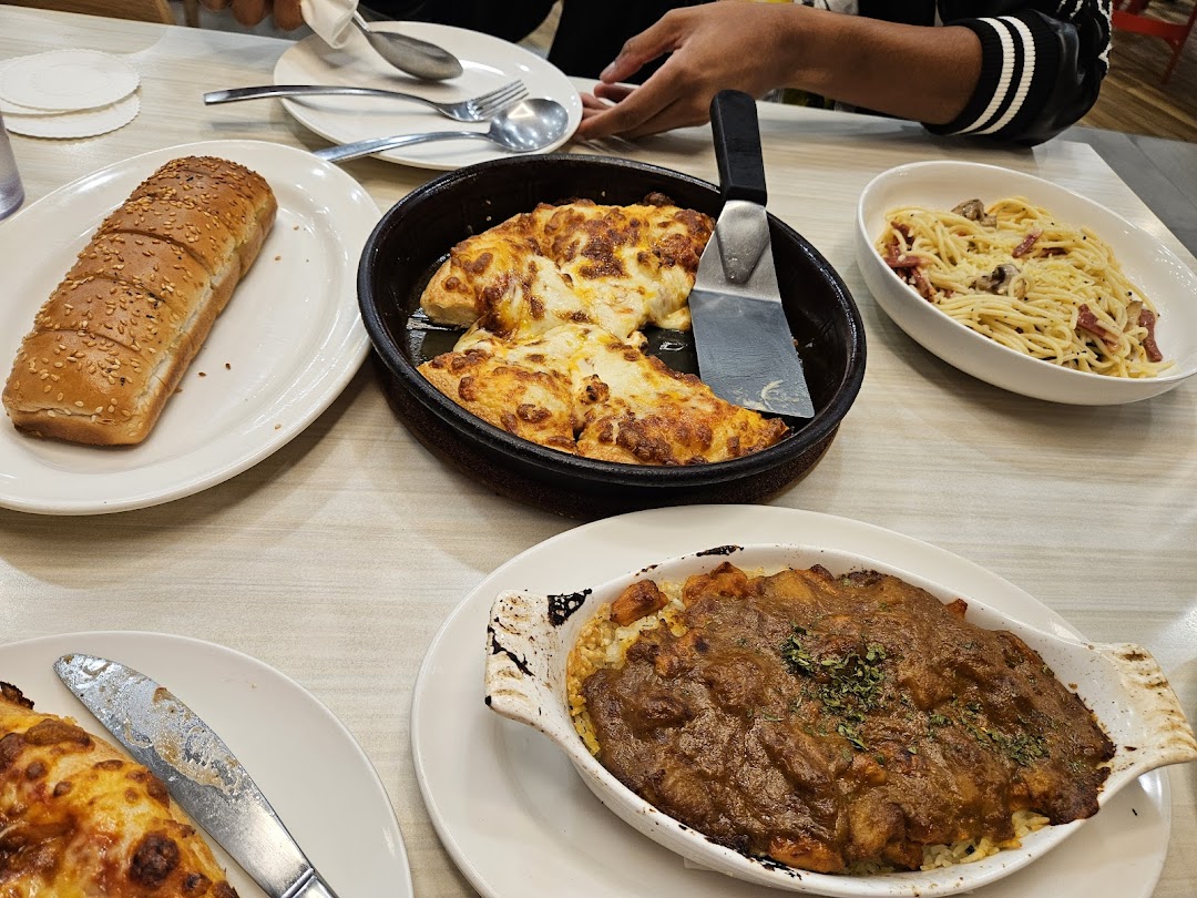 A table filled with various Pizza Hut dishes, including pizza, pasta, and a baked rice dish.