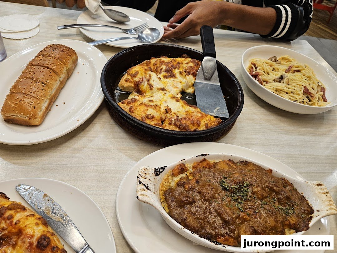 A table filled with various Pizza Hut dishes, including pizza, pasta, and a baked rice dish.
