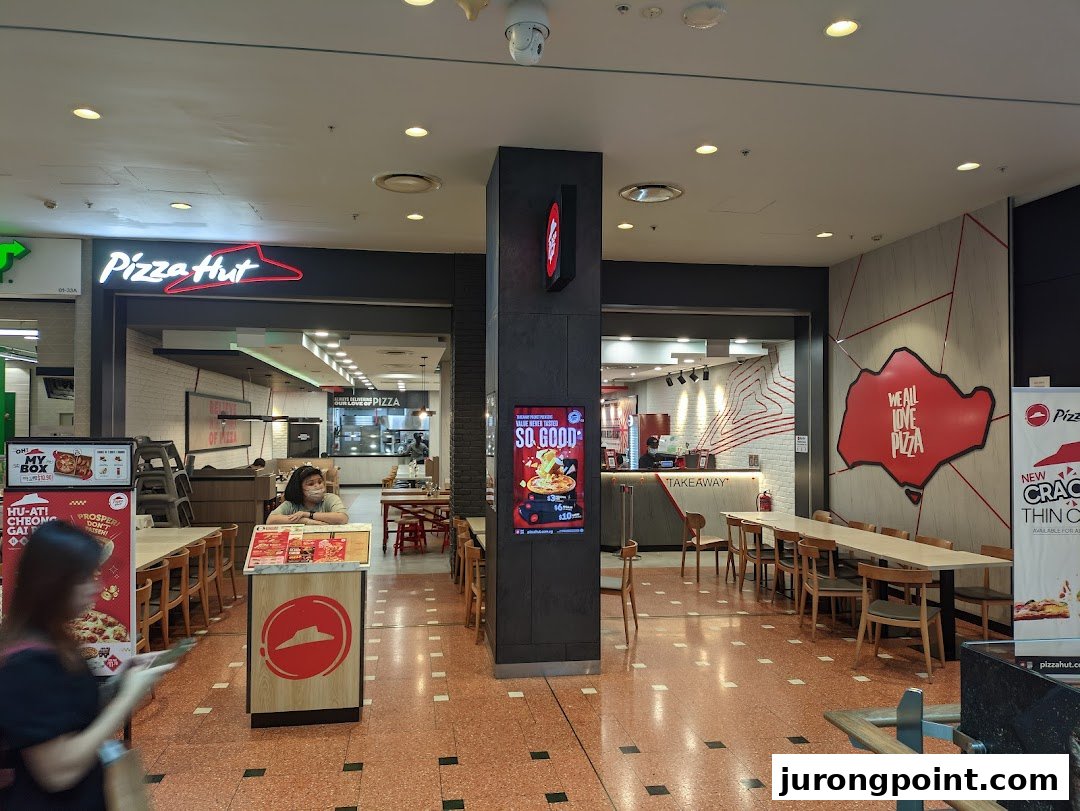 The inviting entrance and interior of a Pizza Hut restaurant with seating and a takeaway counter.