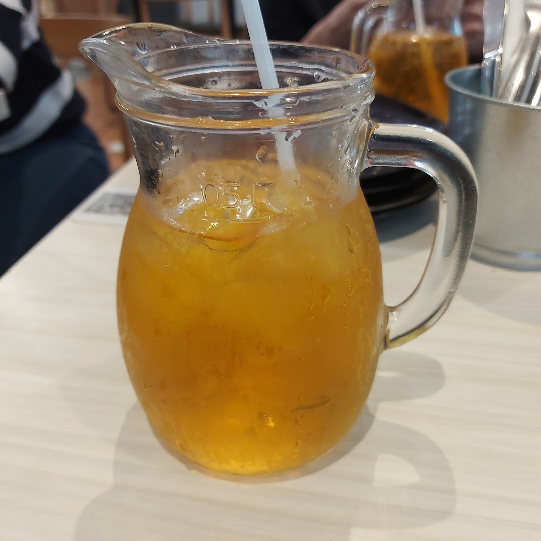 A glass pitcher filled with refreshing iced tea and ice cubes, with a straw, on a table.