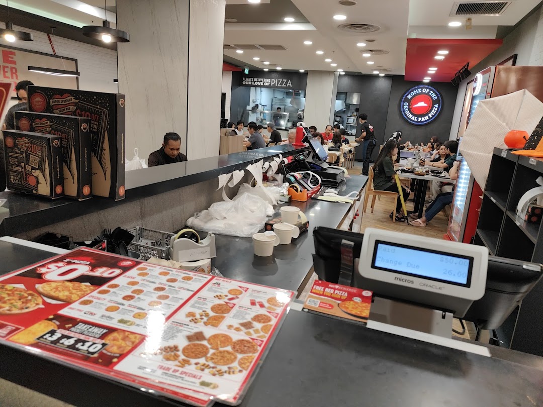 Interior view of a bustling Pizza Hut restaurant with customers dining and a service counter.