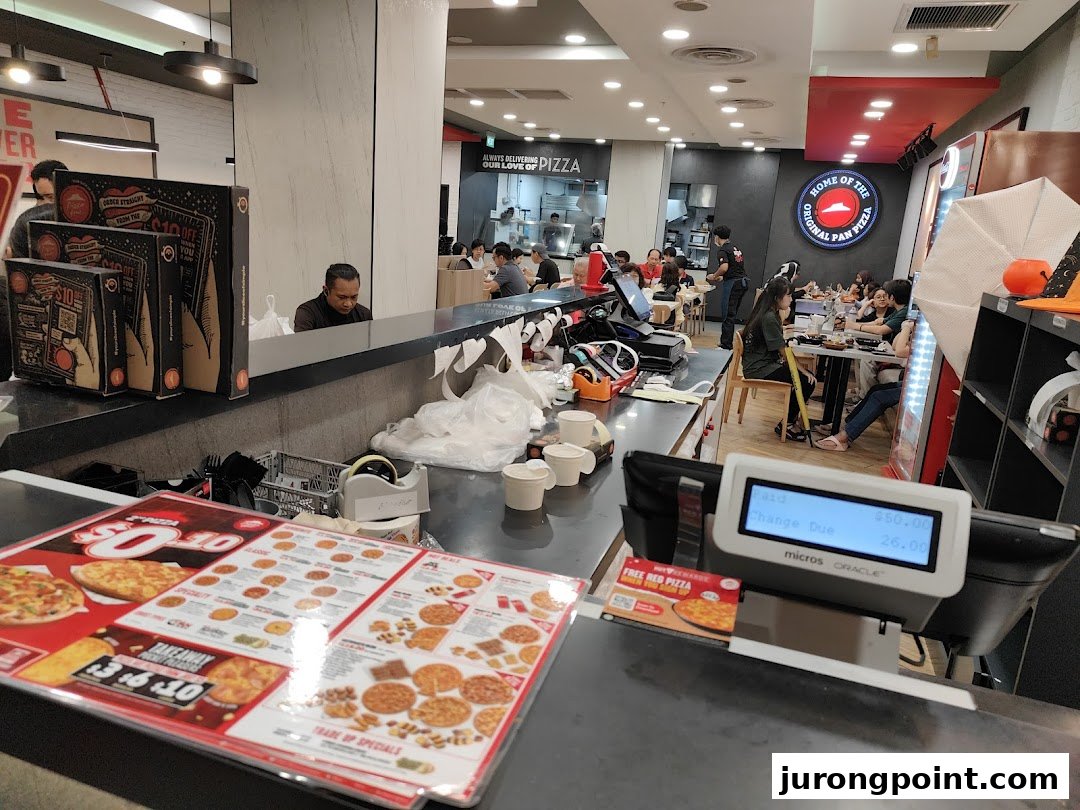 Interior view of a bustling Pizza Hut restaurant with customers dining and a service counter.