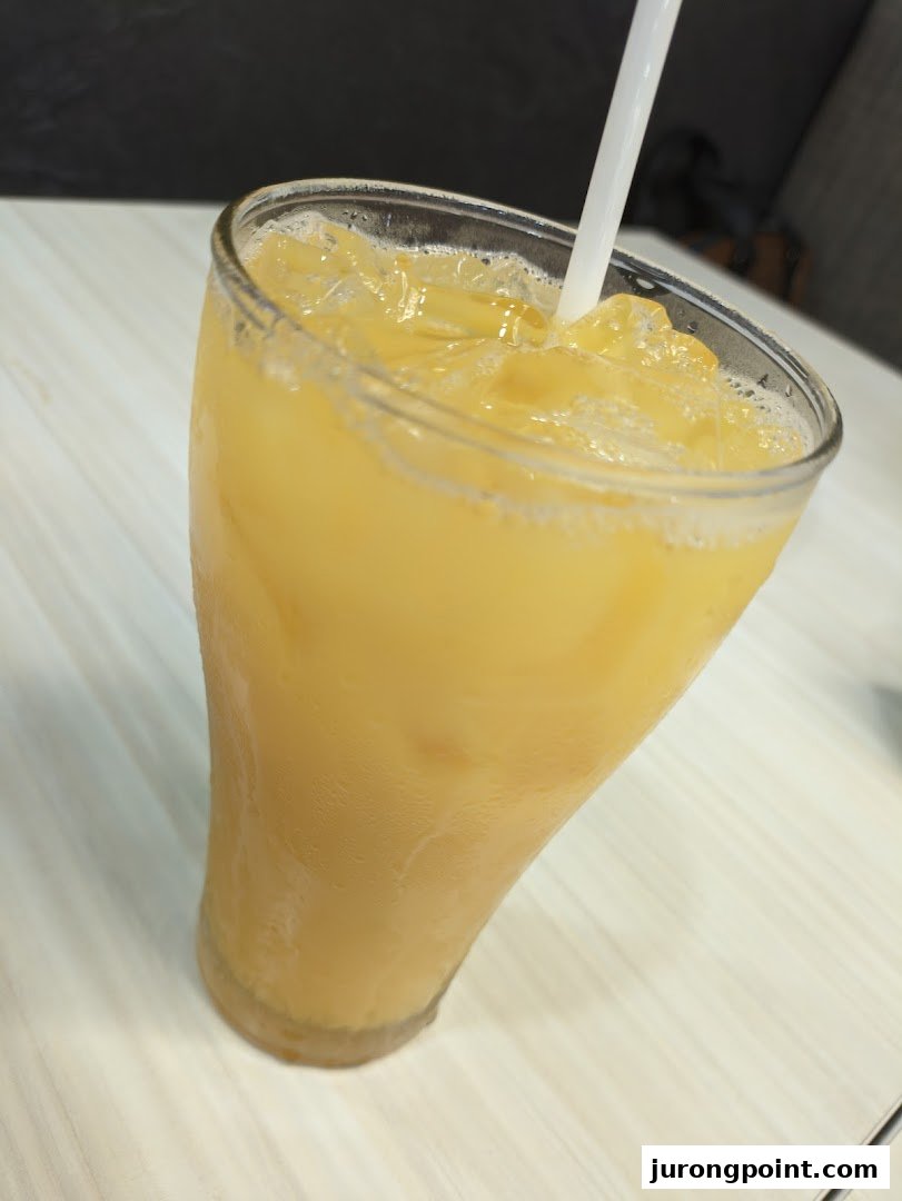 A refreshing glass of iced orange-colored beverage with a white straw on a light-colored table.