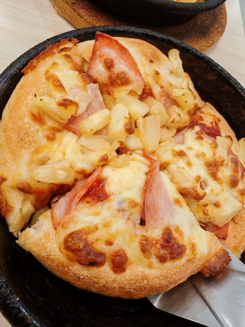 A close-up of a freshly baked Hawaiian pizza with ham, pineapple, and melted cheese in a pan.