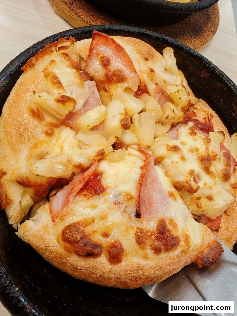 A close-up of a freshly baked Hawaiian pizza with ham, pineapple, and melted cheese in a pan.