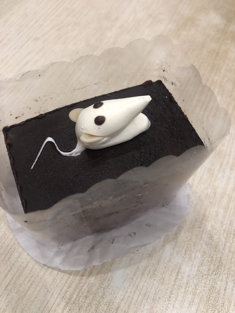 A chocolate cake decorated with a cute white mouse, presented in a paper liner.