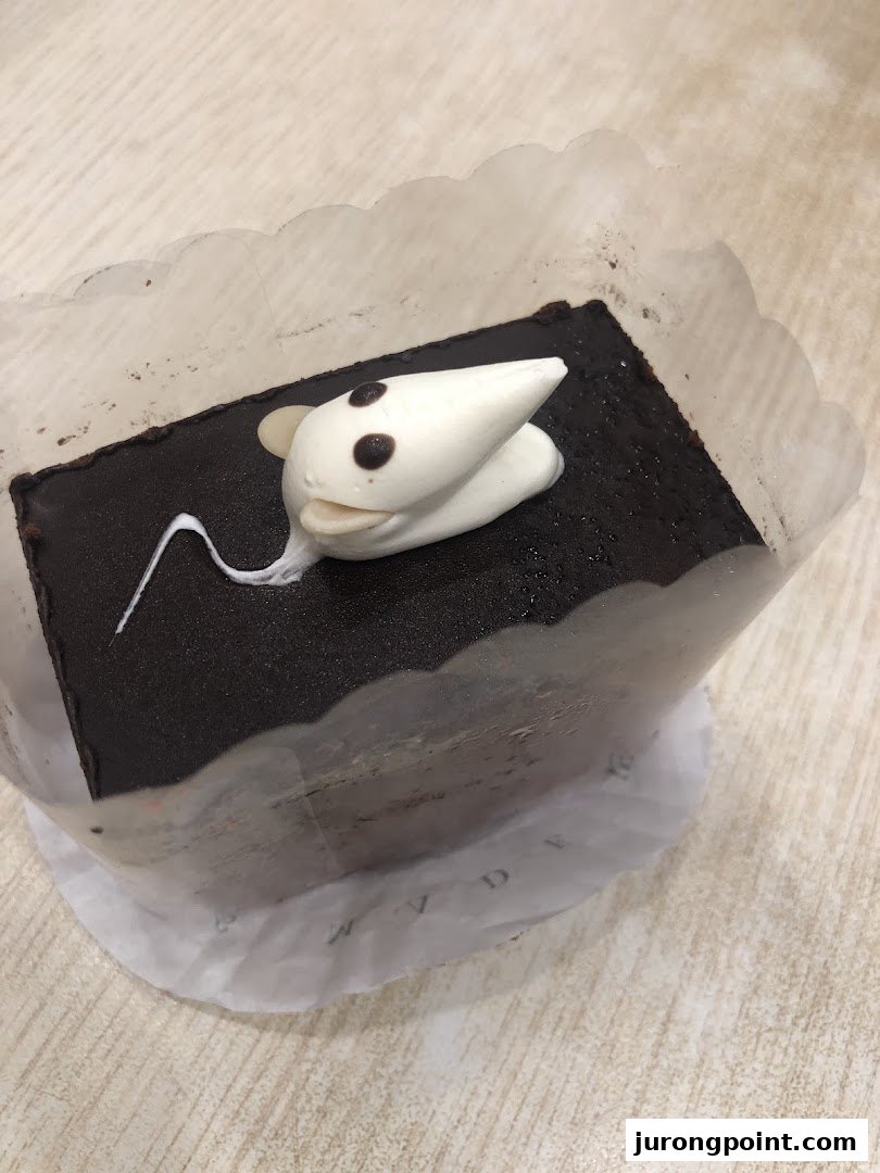 A chocolate cake decorated with a cute white mouse, presented in a paper liner.