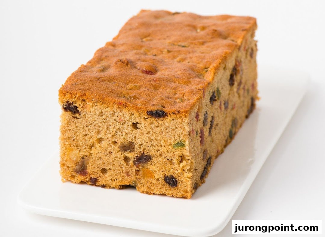 A delicious fruit cake loaf, rich with dried fruits, presented on a clean white rectangular plate.