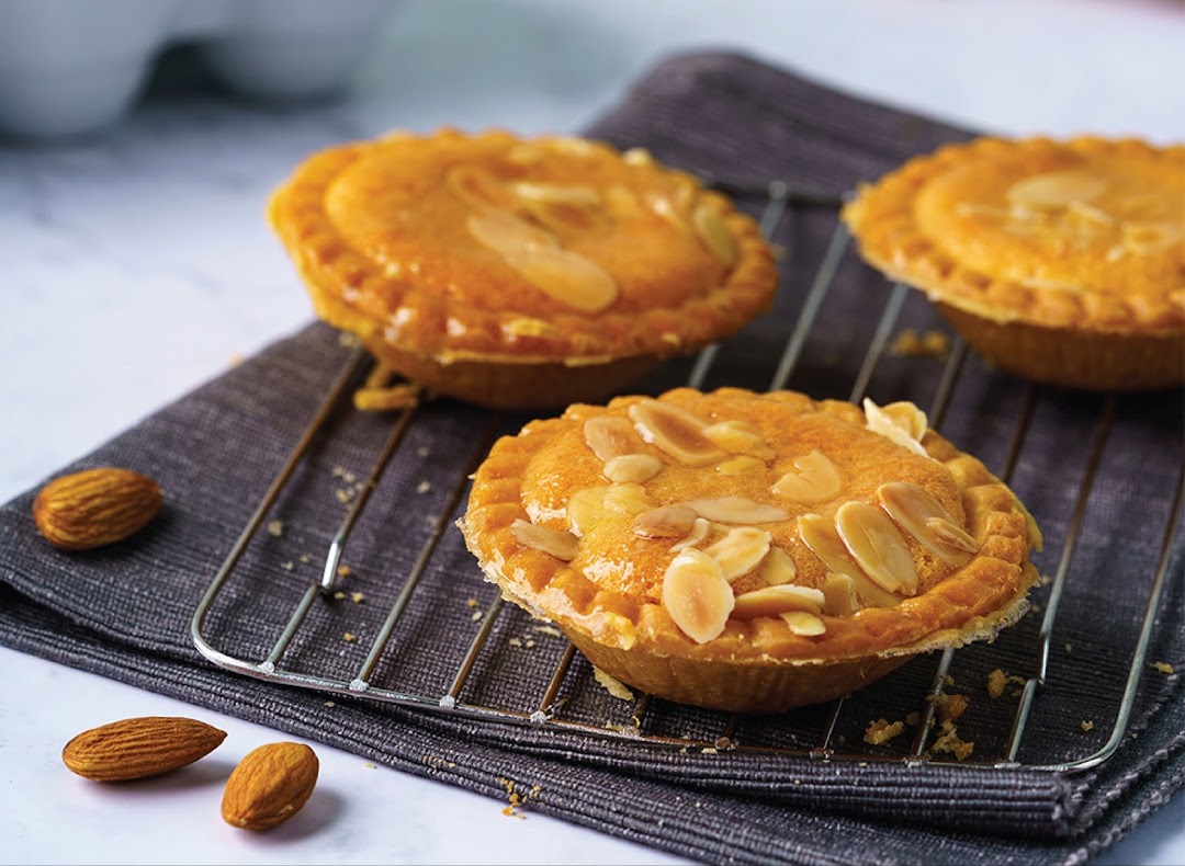 Three golden almond tarts with flaked almonds on a cooling rack, alongside whole almonds.