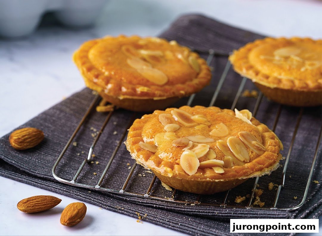 Three golden almond tarts with flaked almonds on a cooling rack, alongside whole almonds.