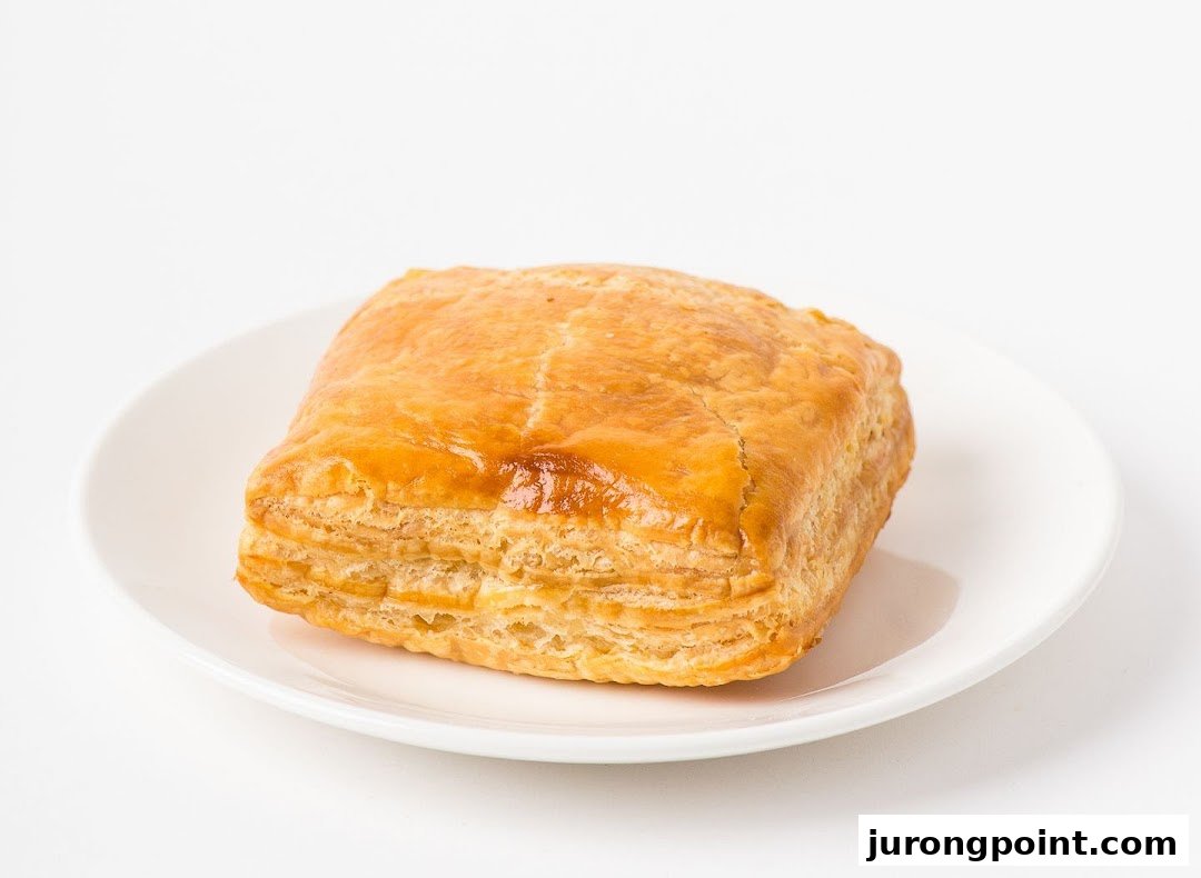 A golden-brown, flaky puff pastry sits on a clean white plate against a bright background.