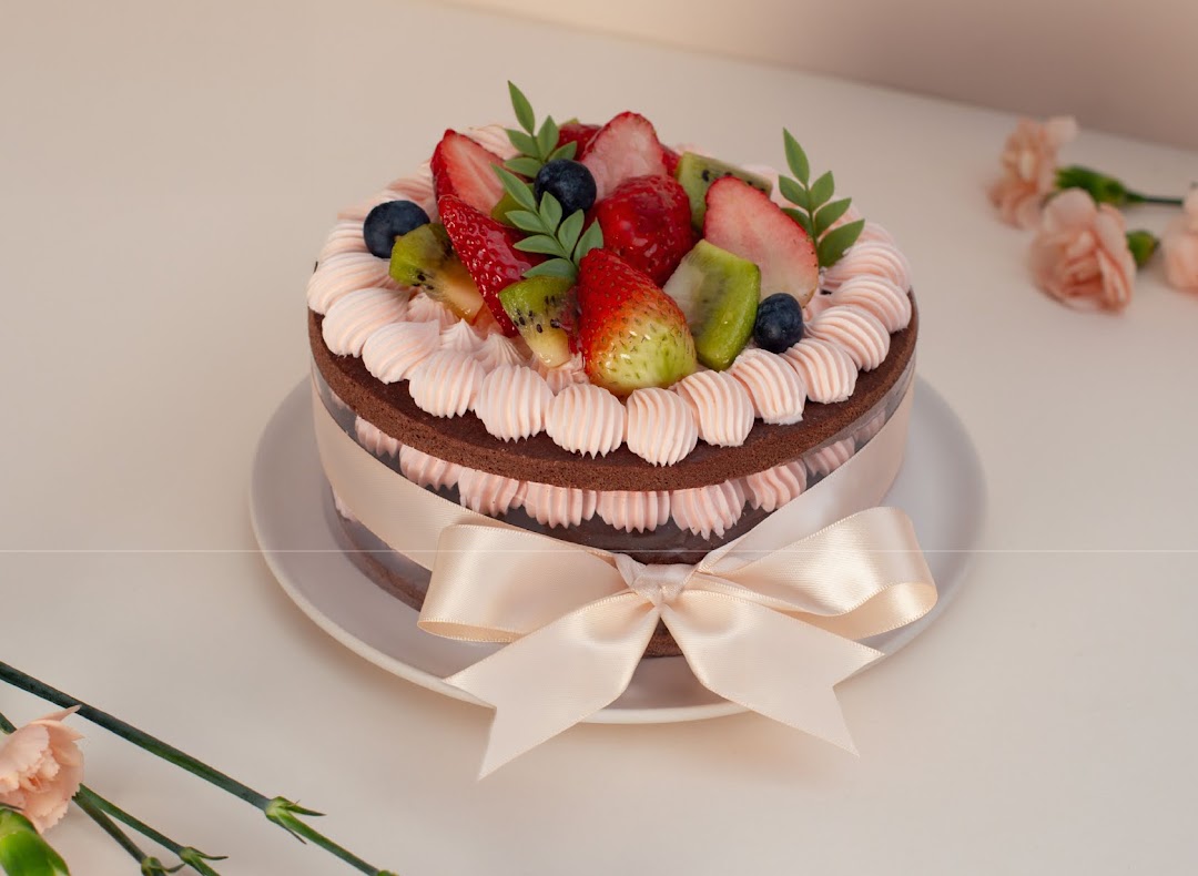 A chocolate cake with pink frosting, fresh berries, and kiwi, elegantly tied with a ribbon.