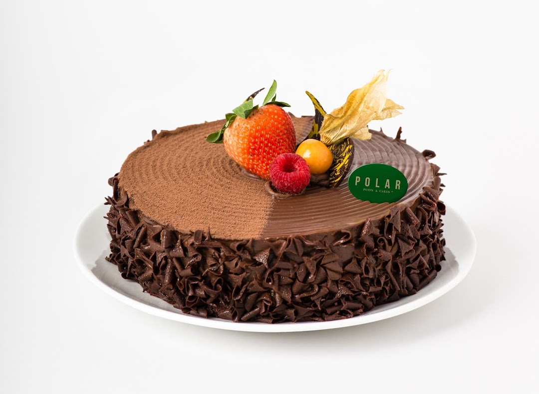 A decadent chocolate cake from Polar Puffs & Cakes, adorned with fresh berries and a brand tag.