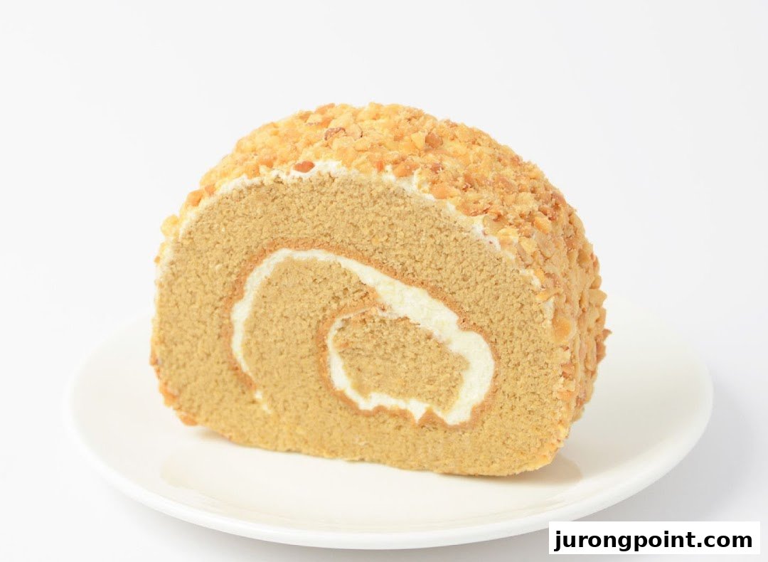 A delicious slice of cake roll with cream filling and nut topping on a white plate.