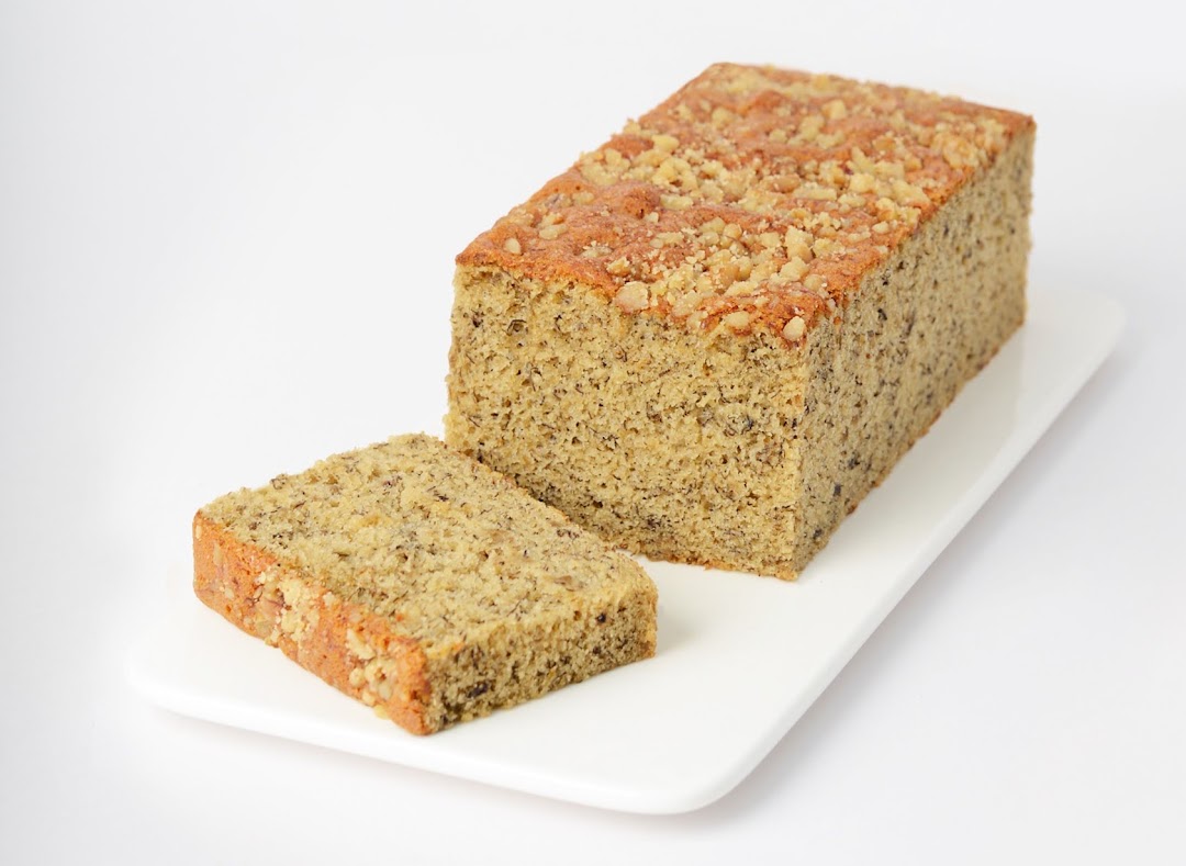 A delicious loaf of banana bread with a slice cut, topped with nuts, on a white platter.